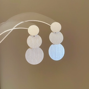 Brushed silver triple circle drop earrings for women on a transparent jewelry display stand