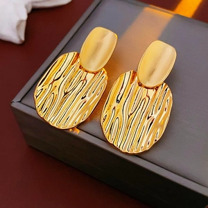 Gros plan de boucles d'oreilles dorées à texture ondulée sur un coffret à bijoux gris