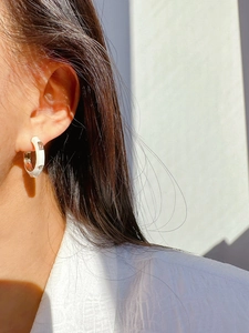 Close-up of white enamel hoop earring with sparkling zircons worn on model ear