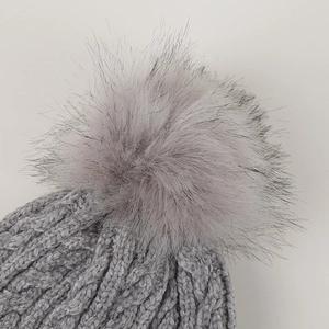 Close-up of thick cable knit texture and fluffy faux fur pom-pom on grey winter beanie