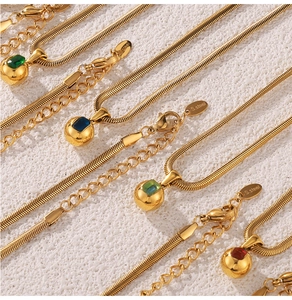 Macro shot of 18k gold-plated snake chains with colorful gemstone orb pendants on stone
