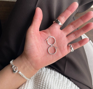 Detailed view of sterling silver hoop earrings and heart charm bracelet on hand