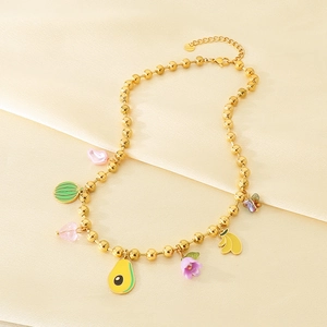 Détail du collier à perles dorées avec breloques émaillées de fruits et fleurs sur tissu