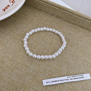 Detail of elegant white faux pearl bracelet laid on a textured tray with decor