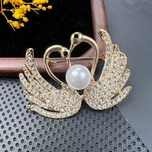 Detail of golden twin swan brooch with crystal pave setting and central large white pearl