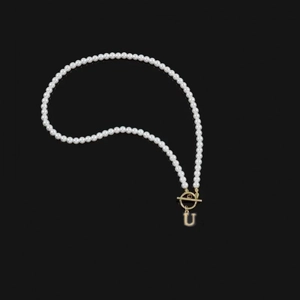 Elegant pearl necklace with golden OT clasp and letter U pendant on black background