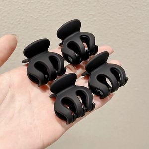 Set of four matte black mini hair claw clips held by hand for elegant hairstyle styling