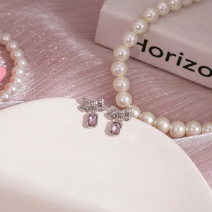 Détail des boucles d'oreilles nœud en argent avec zircons violets sur céramique blanche