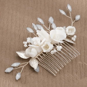 Detail showing white ceramic flowers, silver leaves, and blue beads on a bridal hair comb
