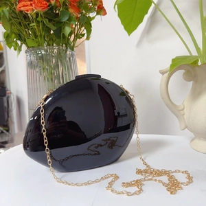Close-up of sleek black oval acrylic evening clutch with gold metal chain strap