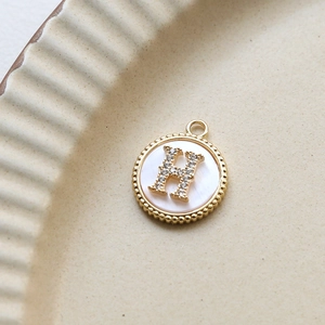 Detailed shot of a gold-plated shell pendant with H-letter zircon inlay on a ceramic tray
