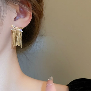 Macro view of gold bow earrings with crystal studs and long tassel chain fringe