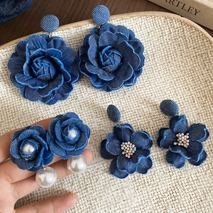 Close-up of handmade denim flower earrings with pearls and beads on a textured tray