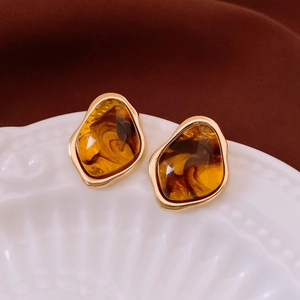 Close-up of irregular amber resin stud earrings with gold trim on a white ceramic plate