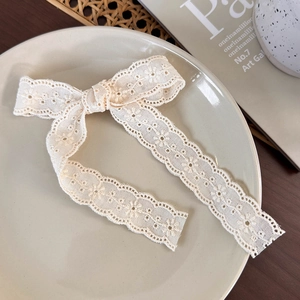 Detailed close-up of a cream lace bow hair clip with floral embroidery on a ceramic plate