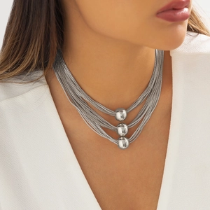 Detail of silver layered chain necklace with geometric ball pendants on white blazer