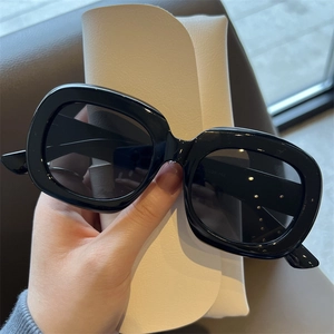 Detailansicht einer schwarzen Sonnenbrille mit Gravur und weißem Lederetui im Fokus