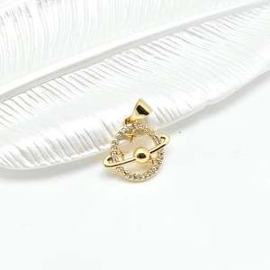 Golden planet charm pendant with sparkling cubic zirconia on a feather tray