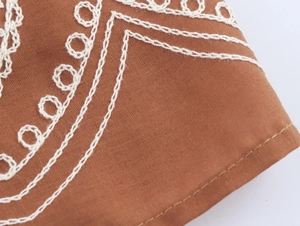 Gros plan d'une broderie à la chaîne blanche sur tissu en lin marron de style ethnique