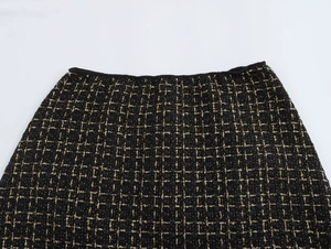 Dettaglio ravvicinato del tessuto tweed a quadri nero e oro e del cinturino della gonna