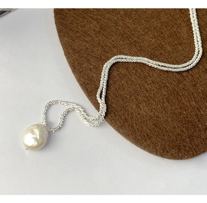 Close-up of S925 silver chain with unique baroque pearl pendant on textured surface
