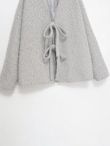 Detail der hellgrauen Wolljacke mit strukturierter Wolle und Schleifenverschluss