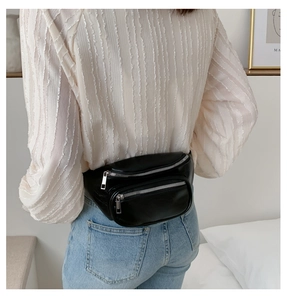 Detail view of a black PU leather waist bag with double silver zippers worn by a model