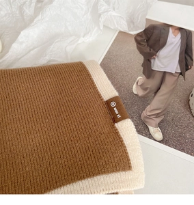 Detailed view of white and beige knit scarf featuring a brown leather brand logo label