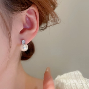 Close-up of pearl drop earrings with square zircon stud worn on ear for elegant style