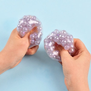 Close-up of hands squeezing a clear stress relief ball filled with colorful purple beads