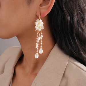 Detail of floral tassel earrings with white petals, gold chains, and shell charms