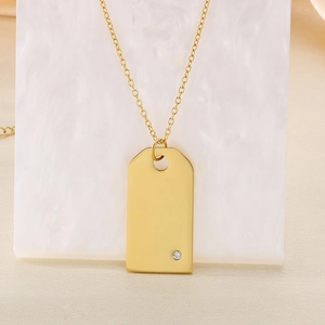 Gros plan d'un pendentif rectangulaire doré avec petit diamant sur support marbre