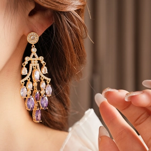 Close-up of elegant gold long tassel earrings with purple gradient crystals on ear