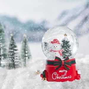 Close-up of Christmas snow globe with snowman, green tree, and red bell-decorated base