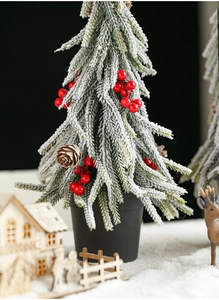 Close-up of snow-flocked mini Christmas tree with pine cones and red berries on wooden base