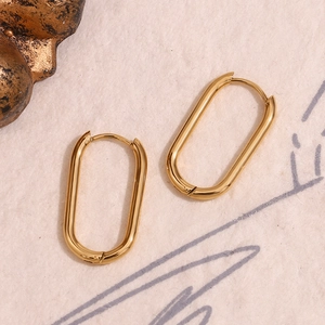 Detailed close-up of oval gold earrings with a high-polished 18K finish on fiber texture