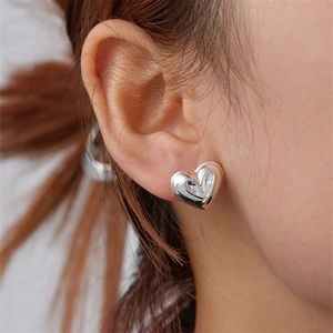 Close-up of polished silver heart stud earrings worn on ear with mirror finish