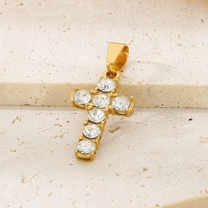 Detail shot of a gold-plated cross pendant with six sparkling diamonds on a stone surface