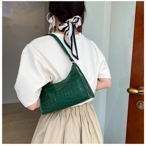 Detail of dark green crocodile texture shoulder bag worn by a model in a minimal setting