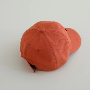 Détail des perforations laser respirantes sur la casquette de sport orange à séchage rapide