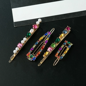 Détail de quatre barrettes en alliage doré avec strass colorés et perles sur fond noir