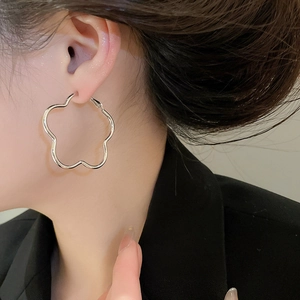 Close-up of elegant silver hollow flower hoop earrings worn by a model in a black blazer