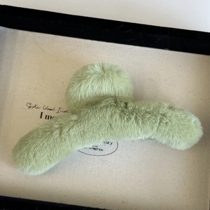 Detail shot of a soft plush green hair claw clip with faux fur texture for winter styling