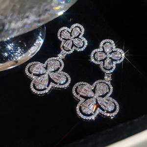 Close-up of sparkling silver clover earrings with inlaid zircons on black velvet background