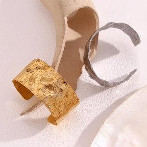 Detailed view of 18K gold hammered texture on open wide bangle with water droplets