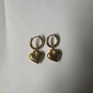 Detail of gold heart-shaped dangle earrings with circular ear clips on white background
