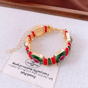 Detailed close-up of gold bracelet with green enamel and pink gemstone on fabric