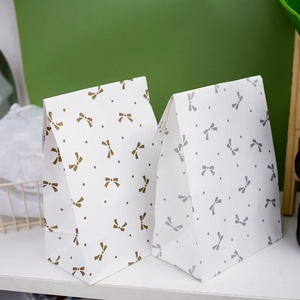 Detail of white paper gift bags with gold and silver bow prints for candy packaging