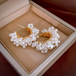 Close-up of vintage C-shaped pearl earrings with gold base in a beige jewelry box
