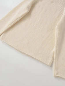 Detail eines cremefarbenen Strickpullovers mit Seitenschlitz und weicher Textur